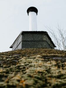 Uneven shingles and exposed flashing visible on a residential roof beside a damp attic ceiling stain.